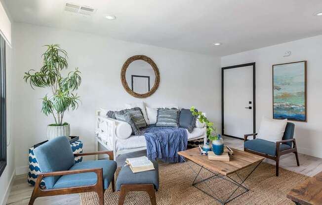 A living room with a white couch, blue chairs, and a painting on the wall.
