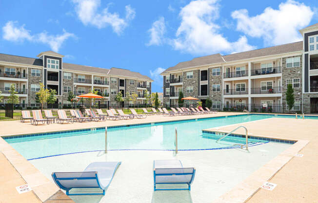 a swimming pool with lounge chairs in front of an apartment building