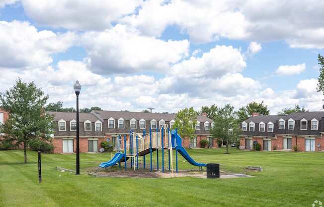 A playground with a blue slide in the middle of a grassy area.