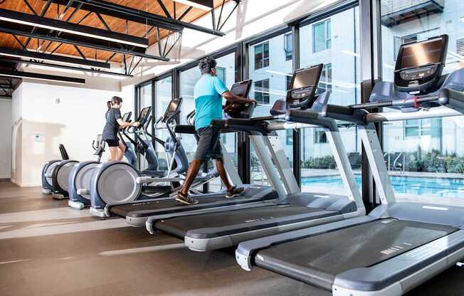 A gym with people exercising on treadmills and elliptical machines.
