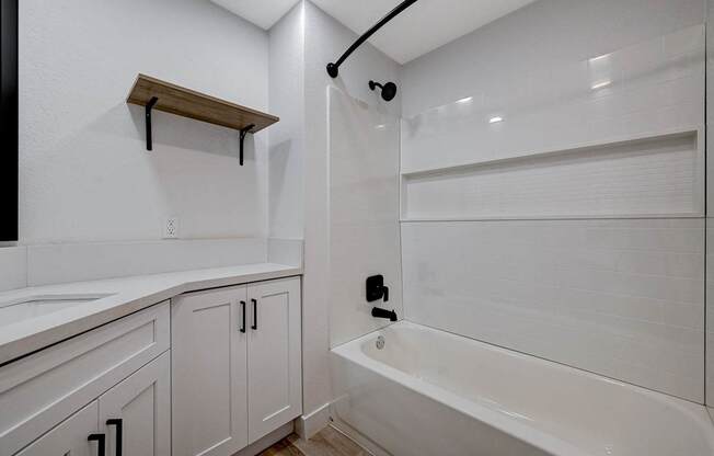 A white bathroom with a tub, sink, and shelving.