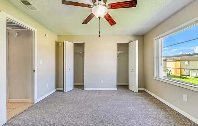 A room with a ceiling fan and a window overlooking a building.