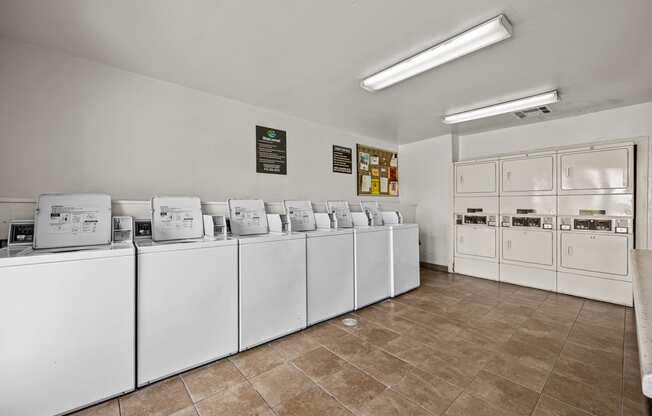 a row of white washers and dryers in a laundry room with tile floor