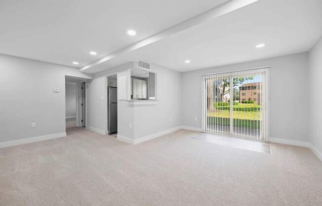 A spacious room with a carpeted floor and a window with blinds.