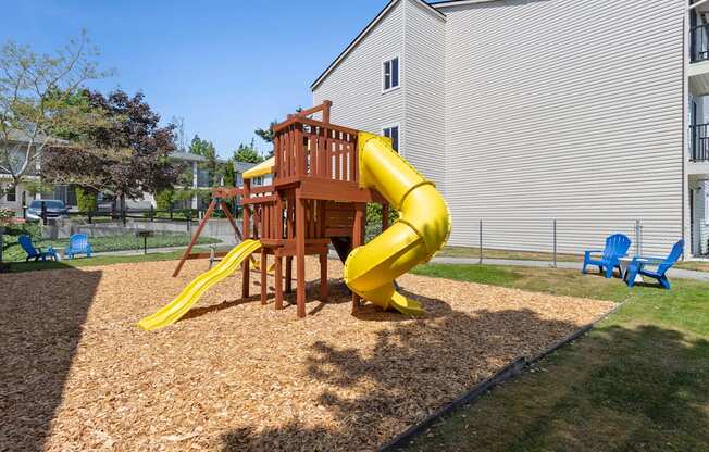 Property Playground with a yellow slide and a wooden deck with blue chairs in an outdoor area at Park Edmonds Apartment Homes, Edmonds, Washington