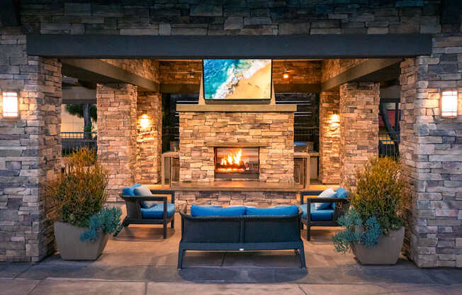 A cozy outdoor seating area with a stone fireplace and cushioned chairs.
