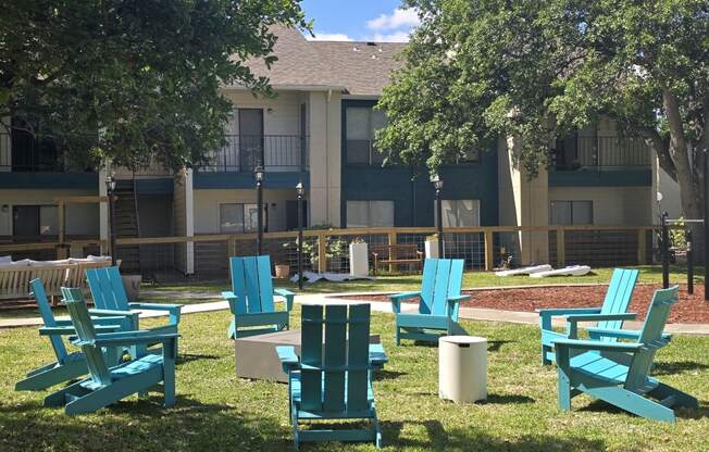 an outdoor lounge area with chairs and trees in front of an apartment building