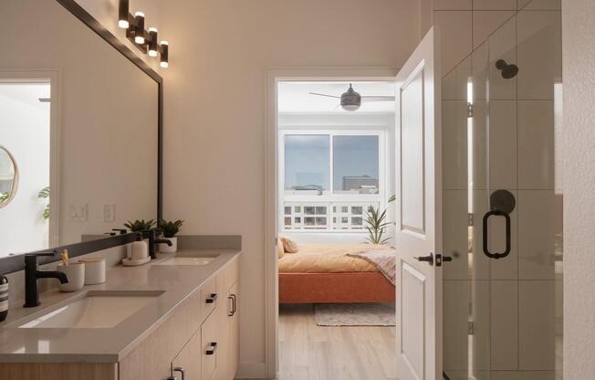 Dual sinks, matte black fixtures, and a glass-enclosed shower create a clean, connected bath that flows seamlessly into the bedroom.