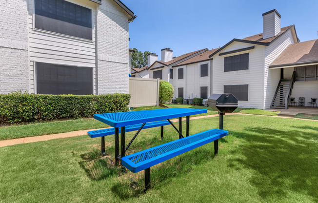 a blue picnic table sits in the middle of a grassy yard in front of a white