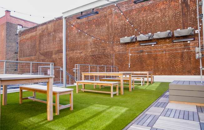 a row of tables and benches on a lawn in front of a brick wall at East 4th Street, Cleveland, 44115