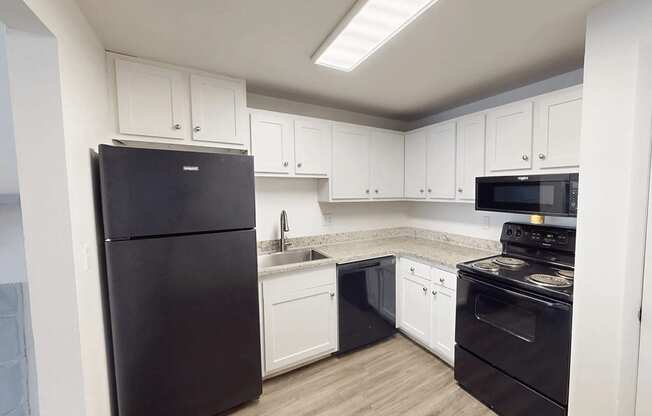 A black refrigerator is in a kitchen with white cabinets.
