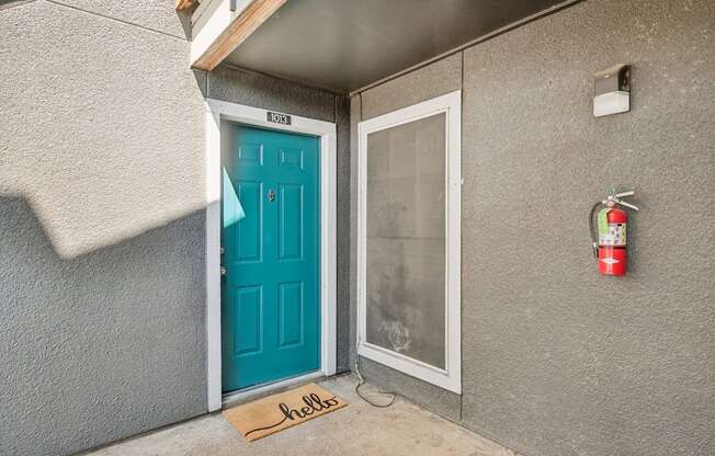 A blue door with a glass window and a mat that says