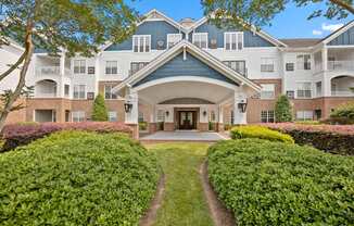 A large building with a blue roof and white walls is surrounded by green bushes.