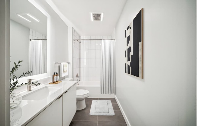 A bathroom with a white sink, toilet, and bathtub with a grey floor and a white wall.