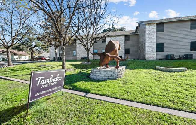 a statue of a bull in the grass in front of a building