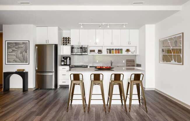 a kitchen with white cabinets and a bar with three bar stools