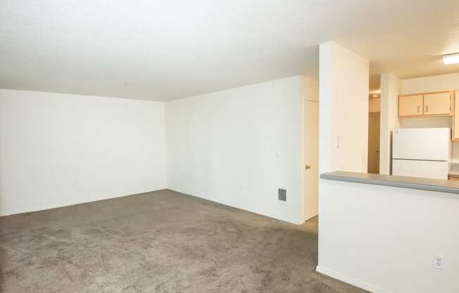 an empty living room with a kitchen in the background