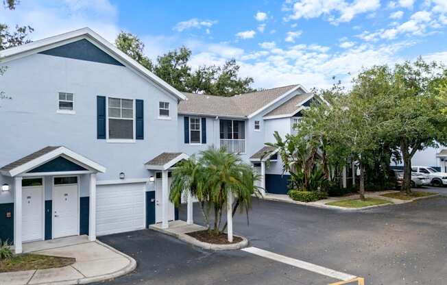 A white building with a blue roof and a tree in front.