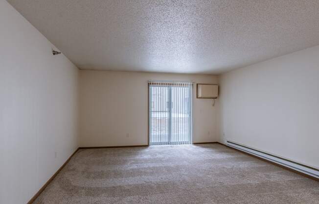 an empty living room with a sliding glass door to a balcony. Fargo, ND Eagle Run Apartments