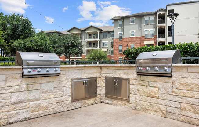 Two outdoor grills are built into a stone wall.