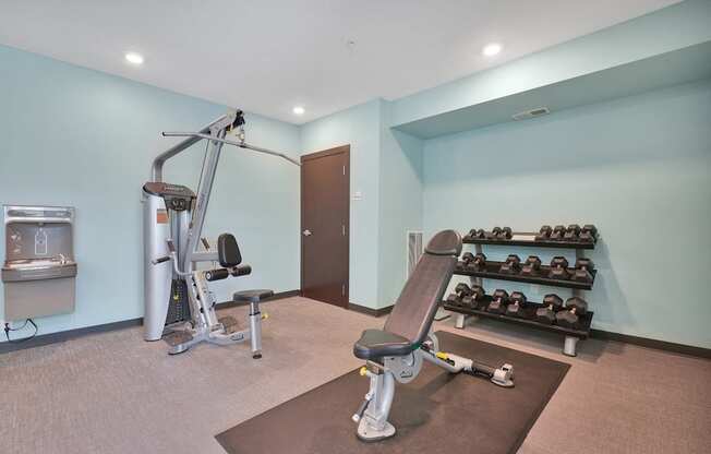 A gym room with a variety of equipment including a treadmill, weights, and a bench press.