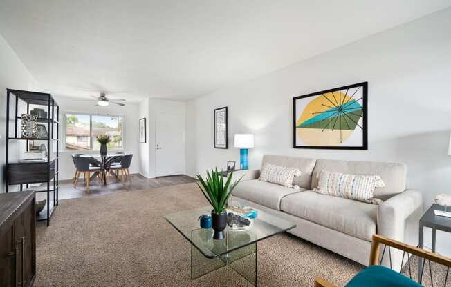 a living room with a couch coffee table and a dining room table in the background