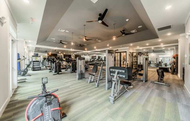 a gym with cardio machines and weights on the floor and a ceiling fan