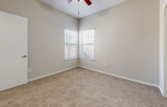 an empty bedroom with two windows and a ceiling fan