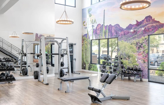 A gym with a variety of equipment and a large window showing a view of the outdoors.