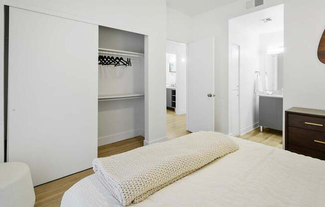 A white bed with a white pillow is in the foreground of a room with a white wardrobe and a white door.