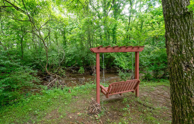 A wooden swing set is situated in a green forest at The Retreat at Indian Lake Apartments in Hendersonville TN.