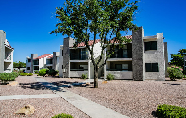 an exterior view of an apartment building with a gravel courtyard and a tree