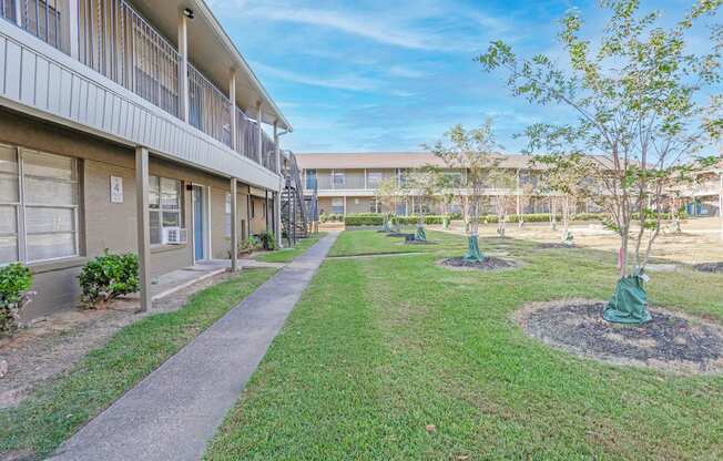 A sunny day at an apartment complex with a clear blue sky and a wide grassy field with young trees at The Creole Apartments in Shreveport, LA