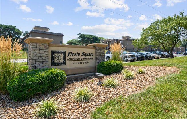 A sign for Flesta Square Apartments is in front of a parking lot.