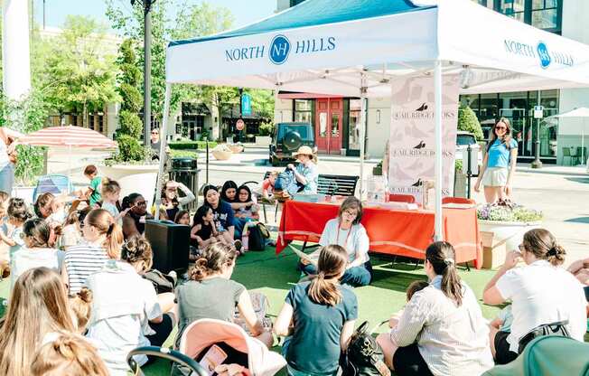A group of people are sitting on the grass in front of a tent with the sign "NORTH Hills" on it.