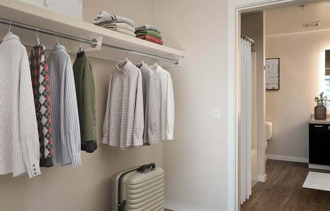 a closet with clothes hanging on a rack and a suitcase