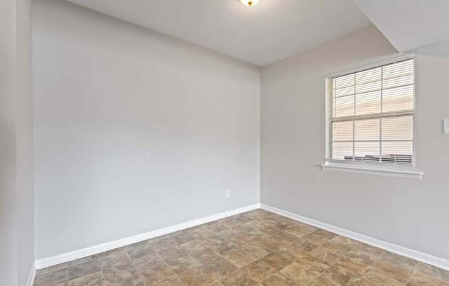an empty living room with a window and a tiled floor