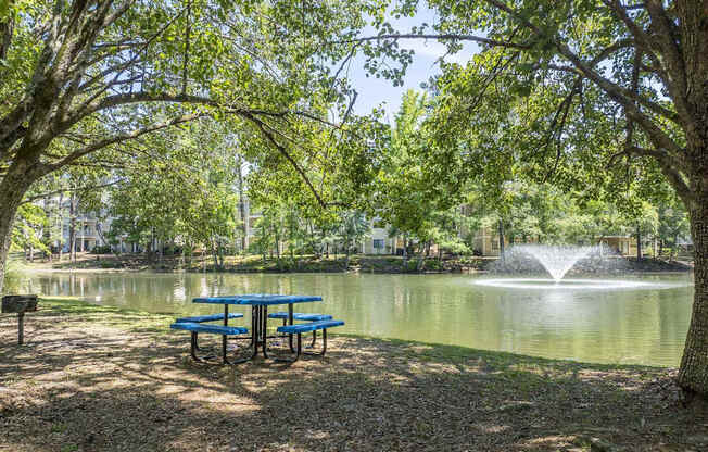 A picnic table is in front of a pond with a fountain.