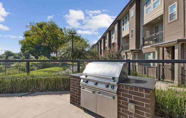 A brick BBQ grill is in the middle of a concrete patio.