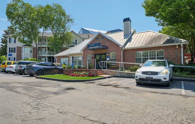 A white car is parked in front of a brick building with a blue sign.
