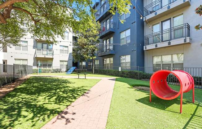 A playground with a red slide in front of apartment buildings.