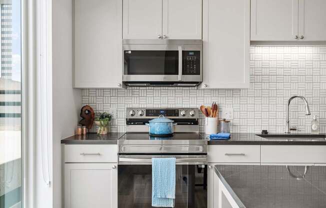 A modern kitchen with white cabinets and a blue towel hanging on the oven.