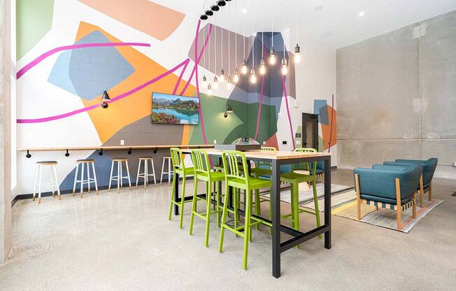A room with a table and chairs in front of a wall with a painting on it.