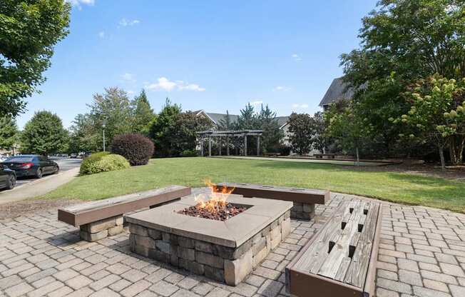 A fire pit in the middle of a brick patio surrounded by benches.
