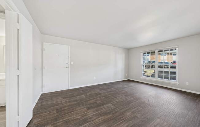 A room with wooden flooring and a window showing a view of a street.