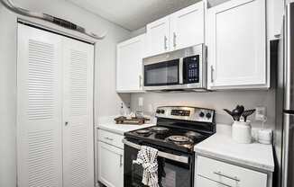 A white kitchen with a black stove top oven and a microwave above it.