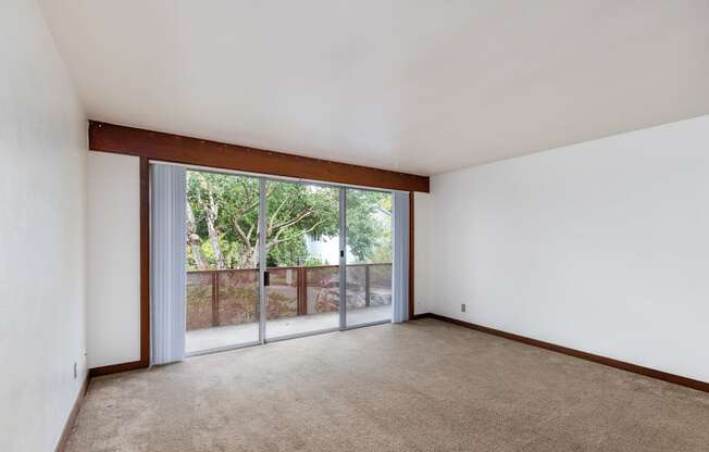 an empty living room with a sliding glass door to a balcony