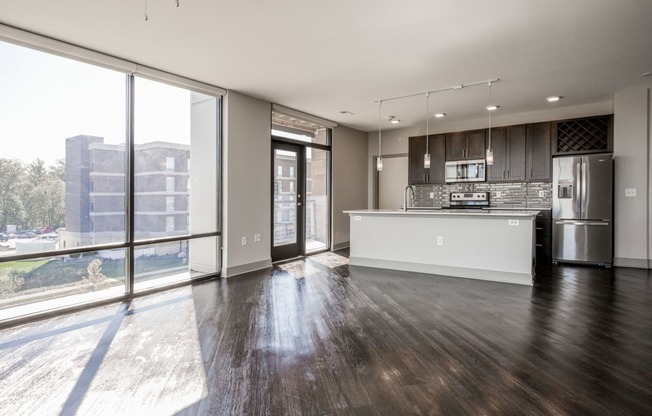 an empty living room with a kitchen and a large window