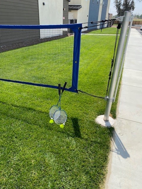 a tennis racket and two tennis balls on the grass next to a fenceat Westbury Apartments, Rancho Cucamonga, 91739