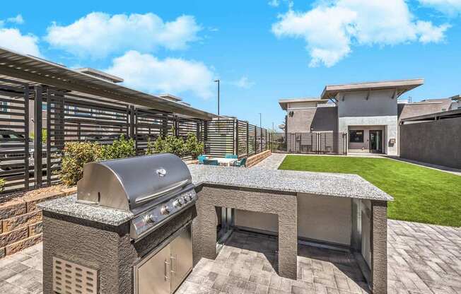 Contemporary outdoor space at Summit on Boulder Apartments with a sleek stainless steel barbecue grill, lush green lawn, and modern seating area under a clear blue sky.
